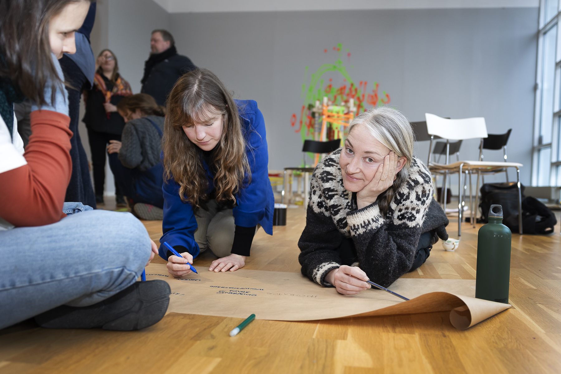 Två personer ligger på golvet och skriver på ett stort papper.